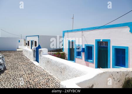 Traditionelle weiß getünchte Häuser mit blauen Akzenten säumen eine kopfsteingepflasterte Straße in Thirasia, Griechenland, eine Szene, die die ruhige Schönheit der Kykladen einfängt Stockfoto