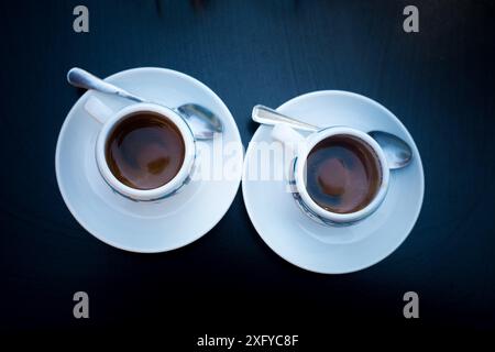 Zwei Tassen Kaffee mit runden weißen Tellern und Teelöffeln auf schwarzem Tisch. Blick von oben. Kaffee am Morgen in der Bar für ein Paar. Kaffee Espresso Stockfoto