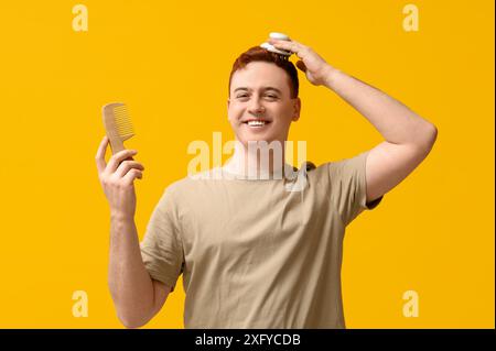 Junger Mann mit Haarkopf-Massagegerät und Kamm auf gelbem Hintergrund Stockfoto