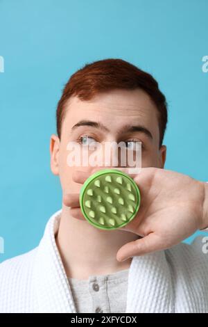 Junger Mann mit Haarkopfmassagegerät auf blauem Hintergrund Stockfoto