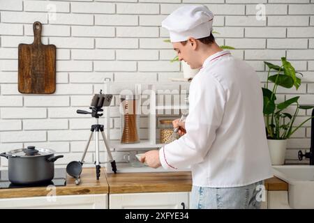 Männlicher Koch mit Schneebesen, der Kochvideo in der Küche aufnimmt Stockfoto