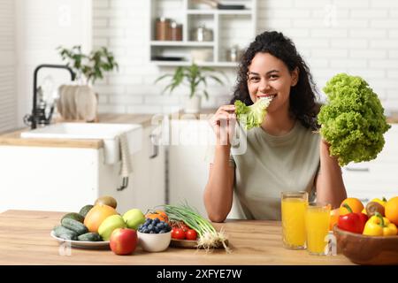 Junge glückliche afroamerikanische Frau mit Gläsern Saft, verschiedenen Gemüse und Früchten in der Küche. Unabhängigkeit vom Fleischtag Stockfoto