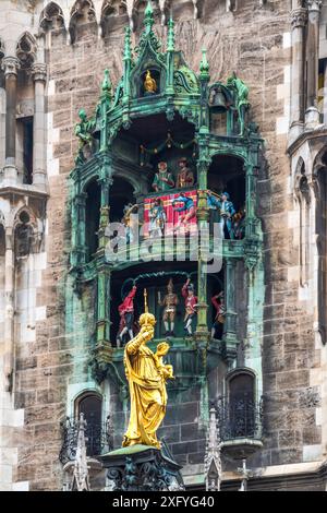 Das Carillon auf dem Münchner Rathaus zeigt eine Szene aus der Hochzeit zwischen Herzog Wilhelm V. und Renate von Lothringen. Die untere Ebene zeigt den Schäffler-Tanz, bei dem sich die Fassmacher nach Überleben der Pestepidemie wieder auf die Straße wagten. Das Carillon besteht aus insgesamt 43 Glocken. Im Vordergrund steht die Mariensäule am Marienplatz Stockfoto