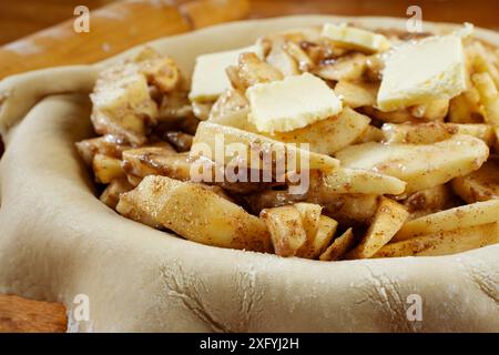 Torte machen. Gerollter Teig über eine Kuchenschale gelegt und mit Apfelscheiben gefüllt, die mit Butter gefüllt sind. Ansicht von oben. Rollstift im Hintergrund. Stockfoto