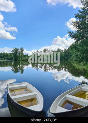 Zwei Kanus sind nach starkem Regen voller Regenwasser und liegen am Ufer eines Sees, die Wolken spiegeln sich im Wasser mit blauem Himmel, Klimawandel, Nordrhein-Westfalen, Deutschland Stockfoto