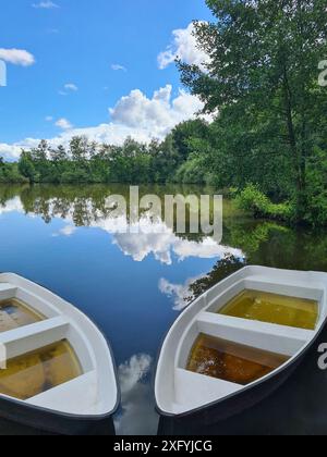 Zwei Kanus sind nach starkem Regen voller Regenwasser und liegen am Ufer eines Sees, die Wolken spiegeln sich im Wasser mit blauem Himmel, Klimawandel, Nordrhein-Westfalen, Deutschland Stockfoto