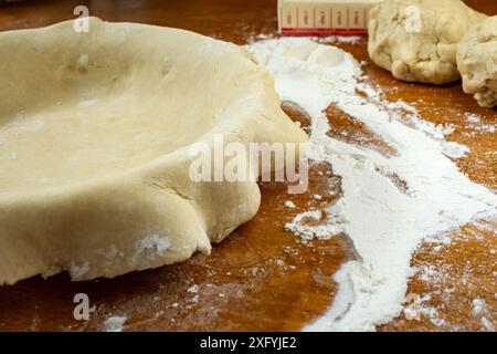 Torte machen. Gerollter Teig, der über eine Kuchenschale gelegt wird. Seitenansicht mit zusätzlichem Teig im Hintergrund. Stockfoto