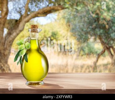 Eine Flasche handgefertigtes Olivenöl steht auf einem Holztisch, hinter einem Olivengarten an einem etwas Bokeh, sonnigen Tag. Stockfoto