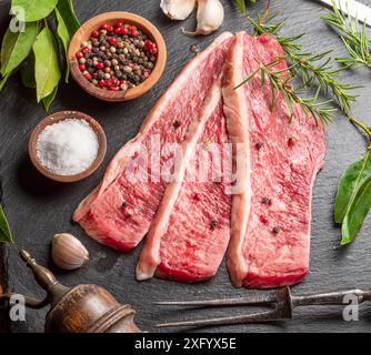 Geschnittenes picanha-Rindfleisch mit Gewürzen und Kräutern auf einem grauen Steinservierbrett mit Blick von oben. Traditionelle portugiesische Küche. Stockfoto