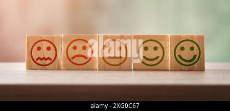 Konzept der Bewertung von Produkten und Dienstleistungen mit Gesichtern mit verschiedenen Emotionen, die auf einer Reihe von Holzwürfeln auf Bank und isoliertem Hintergrund gezeichnet sind. Stockfoto