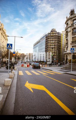 Madrid, Spanien. 1. Juli 2024 Asphaltstraße mit gelben Markierungen für Fahrer, gelber Pfeil links abbiegen, Crosswalk Zebra in einer Stadt. Moderne Gebäude. Stockfoto