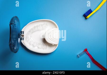 Auf blauem Hintergrund liegt eine weiße Spezialbox für unsichtbare Kunststoffspangen, Aligner, Zahnbürste und kieferorthopädische Bürste Stockfoto