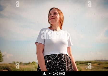 Frau in weißem T-Shirt und schwarzem Rock mit Punktmuster steht im Feld mit Blasen. Stockfoto