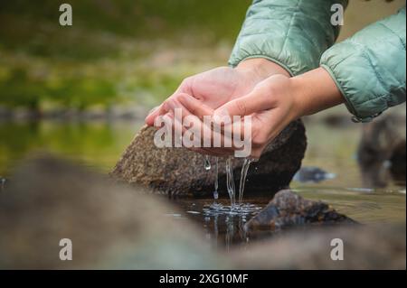 Nahaufnahme von Wassertropfen, die von weiblichen Händen in einen Fluss fallen. Die Hand berührt frisches Wasser. Ein Tourist trinkt Wasser aus einem Reservoir im Stockfoto