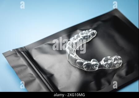 Nahaufnahme, unsichtbare Kunststoffspangen auf einem schwarzen Spezialpaket mit Reißverschluss auf blauem Hintergrund. studio-Aufnahme, Hintergrund der Zahnklinik Stockfoto