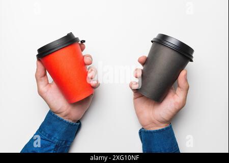 Nahaufnahme, männliche Hände halten zwei Pappbecher mit Kaffee auf weißem Hintergrund, Draufsicht Stockfoto