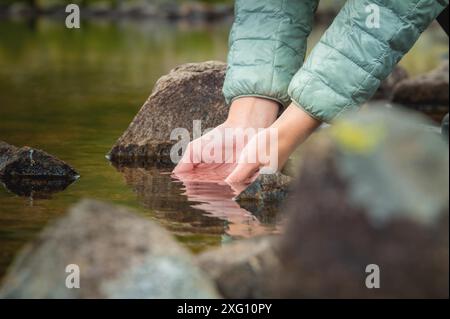 Nahaufnahme von Wassertropfen, die von weiblichen Händen in einen Fluss fallen. Die Hand berührt frisches Wasser. Ein Tourist trinkt Wasser aus einem Reservoir im Stockfoto