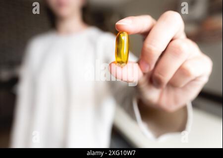 Die Hand einer Frau hält eine Omega-3-Kapsel vor ihrem Hintergrund in einem weißen Pullover, der Hintergrund ist unscharf. Nützliche Fischöl-Kapsel Stockfoto