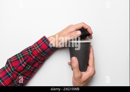Zwei männliche Hände halten beim Öffnen des Kunststoffdeckels einen Einweg-Papierbecher. Nahaufnahme von Kaffee auf weißem Hintergrund, Draufsicht Stockfoto