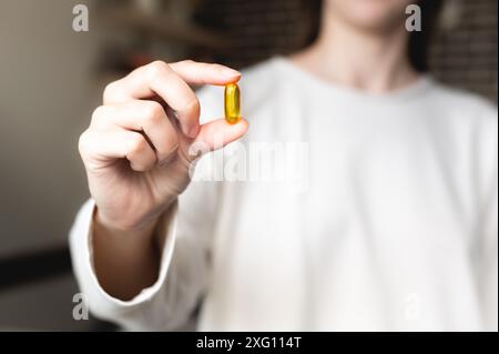 Die Hand einer Frau hält eine Omega-3-Kapsel vor ihrem Hintergrund in einem weißen Pullover, der Hintergrund ist unscharf. Nützliche Fischöl-Kapsel Stockfoto