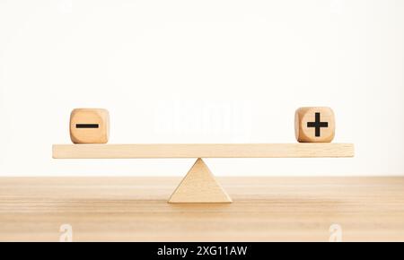 Plus- und Minus-Balance-Konzept. Positive und negative Symbole auf Holzblöcken sind auf einer hölzernen Wippe im Gleichgewicht. Speicherplatz kopieren Stockfoto