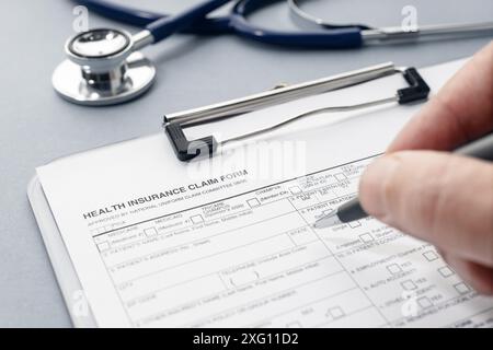 Füllen Sie das Antragsformular für die Krankenversicherung und das Stethoskop auf dem Schreibtisch manuell aus Stockfoto