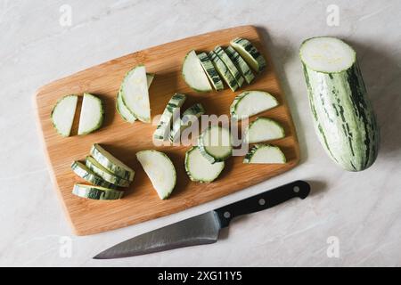 Zucchini in Scheiben geschnitten auf Schneidebrett, Half Squash, Messer auf weißem Tisch, Overhead-Ansicht Stockfoto