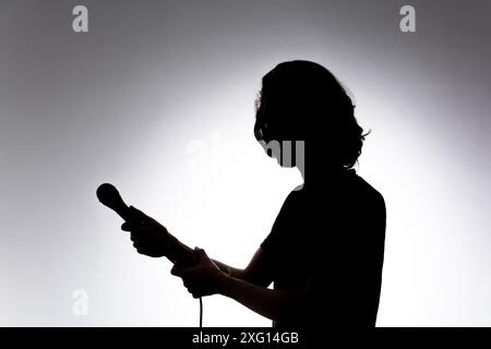 Silhouette eines jungen Sängers, der ein kabelgebundenes Mikrofon hält. Isoliert auf weißem Hintergrund. Stockfoto
