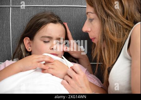 Mutter misst die Temperatur ihrer kranken Tochter. Krankes Kind mit hohem Fieber liegt im Bett und Mutter hält Thermometer. Hochwertige Fotos Stockfoto