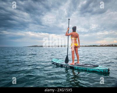 Frau paddelt auf einem Surfbrett unter einem dramatischen Himmel, Sa Rapita, Mallorca, Balearen, Spanien Stockfoto