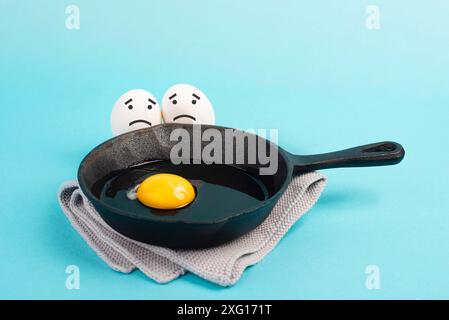 Ein Spiegelei in einer Pfanne, zwei Freunde schauen ihn mit traurigen Gesichtern an, frühstücken am Morgen, komisches Essen, zerbrochene Freundschaft, gesundes Essen Stockfoto