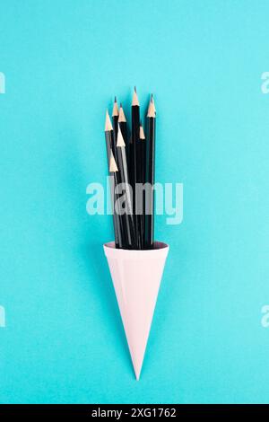 Schwarzer Pencilsin ein Kegel auf blauem Hintergrund, Minimalismus, kreatives, surreales und Bildungskonzept, Kopierraum für Text, pastellfarbene Wand Stockfoto