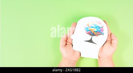 Einen Kopf mit einem bunten Baum in den Händen halten, Symbol für Kreativität, Verbindung zur Natur und positive Emotionen, Leben in einer Traumwelt Stockfoto