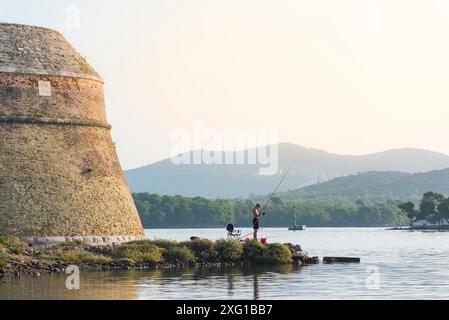 Der junge Mann sitzt und angelt auf dem Kanal sveti Ante in sibenik kroatien Stockfoto