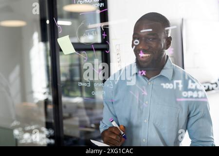 Schreiben auf Glasplatte, lächelnder Geschäftsmann, Ideenfindung im modernen Büro Stockfoto