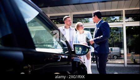 Professionelle Autoverkäuferin, die glückliches hispanisches Paar beim Kauf eines Neuwagens im Händlerbetrieb am sonnigen Tag unterstützt. Stockfoto