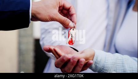 Immobilienmakler übergibt einem jungen Paar Schlüssel für ihr neues Zuhause. Übertragung des Eigentumsrechts abgeschlossen. Stockfoto