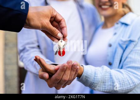 Immobilienmakler übergibt einem jungen Paar Schlüssel für ihr neues Zuhause. Übertragung des Eigentumsrechts abgeschlossen. Stockfoto