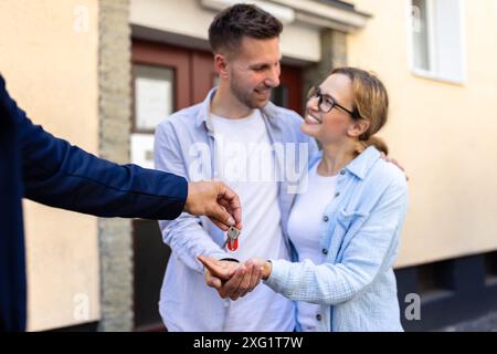 Immobilienmakler übergibt einem jungen Paar Schlüssel für ihr neues Zuhause. Übertragung des Eigentumsrechts abgeschlossen. Stockfoto