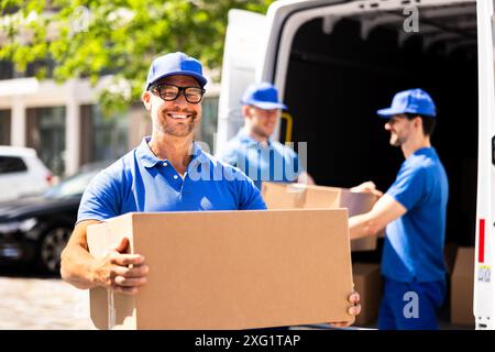Effiziente Liefermänner in blauen Uniformen bringen Geräte in einen Lkw für eine professionelle Umzugsfirma. Stockfoto