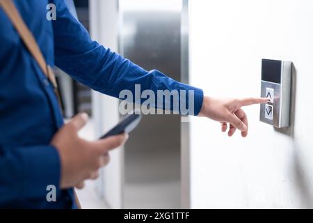 Drücken der Fahrstuhltaste, Person, die das Smartphone hält und im Bürogebäude wartet Stockfoto