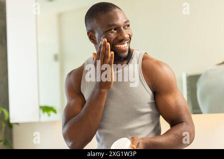 Gesichtscreme auftragen, kräftiger und fitter Mann, der im Badezimmer zu Hause lächelt Stockfoto