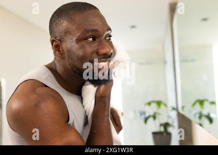 Lächelnder Mann trocknet Gesicht mit Handtuch im Badezimmer zu Hause, genießt Selbstpflege Routine Stockfoto