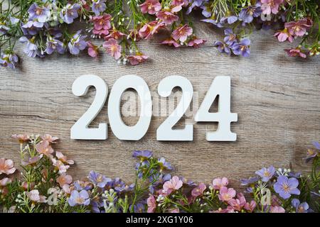 2024 Jahre Zahl mit Blumenrahmen von oben auf hölzernem Hintergrund. Hallo, Willkommen und Goodbye Neujahrskonzept Stockfoto