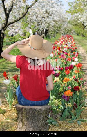 Ein junges Mädchen sitzt auf einem Baumstamm inmitten der Natur und einem Tulpenfeld Stockfoto