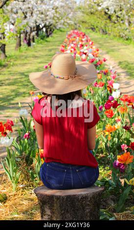 Ein junges Mädchen sitzt auf einem Baumstamm inmitten der Natur und einem Tulpenfeld Stockfoto