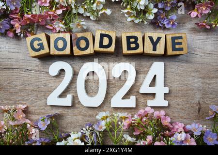 Auf Wiedersehen 2024 Jahre Zahl mit Blumenrahmen von oben auf hölzernem Hintergrund Stockfoto