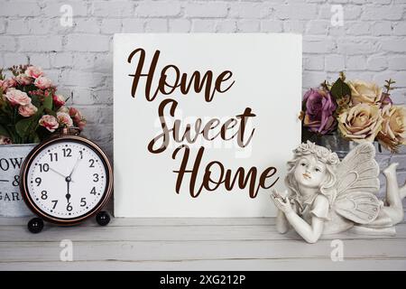 Home Sweet Home Textnachricht mit Wecker und Engel Keramik Puppe Dekoration auf hölzernem Hintergrund Stockfoto