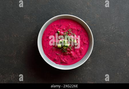 Rübencremesuppe mit Joghurt, Gurken und Dill in Schüssel auf schwarzem Hintergrund. Kalte Sommersuppe. Draufsicht, flach Stockfoto