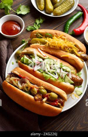 Hot Dogs mit verschiedenen Belägen auf weißem Teller auf Holztisch. Nahansicht Stockfoto